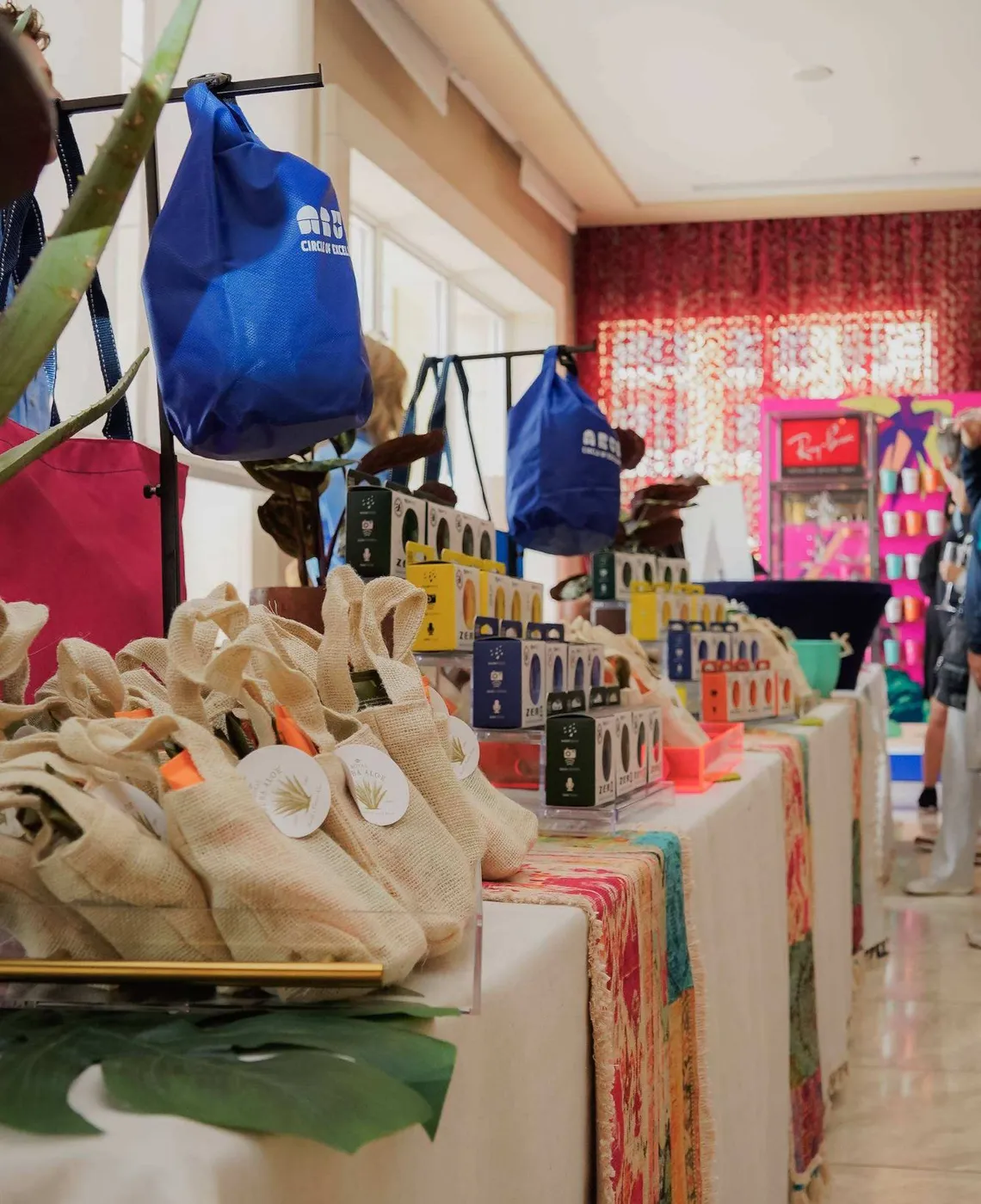 Onsite gifting suite with branded bags, tech accessories and burlap gift pouches on a long display table.