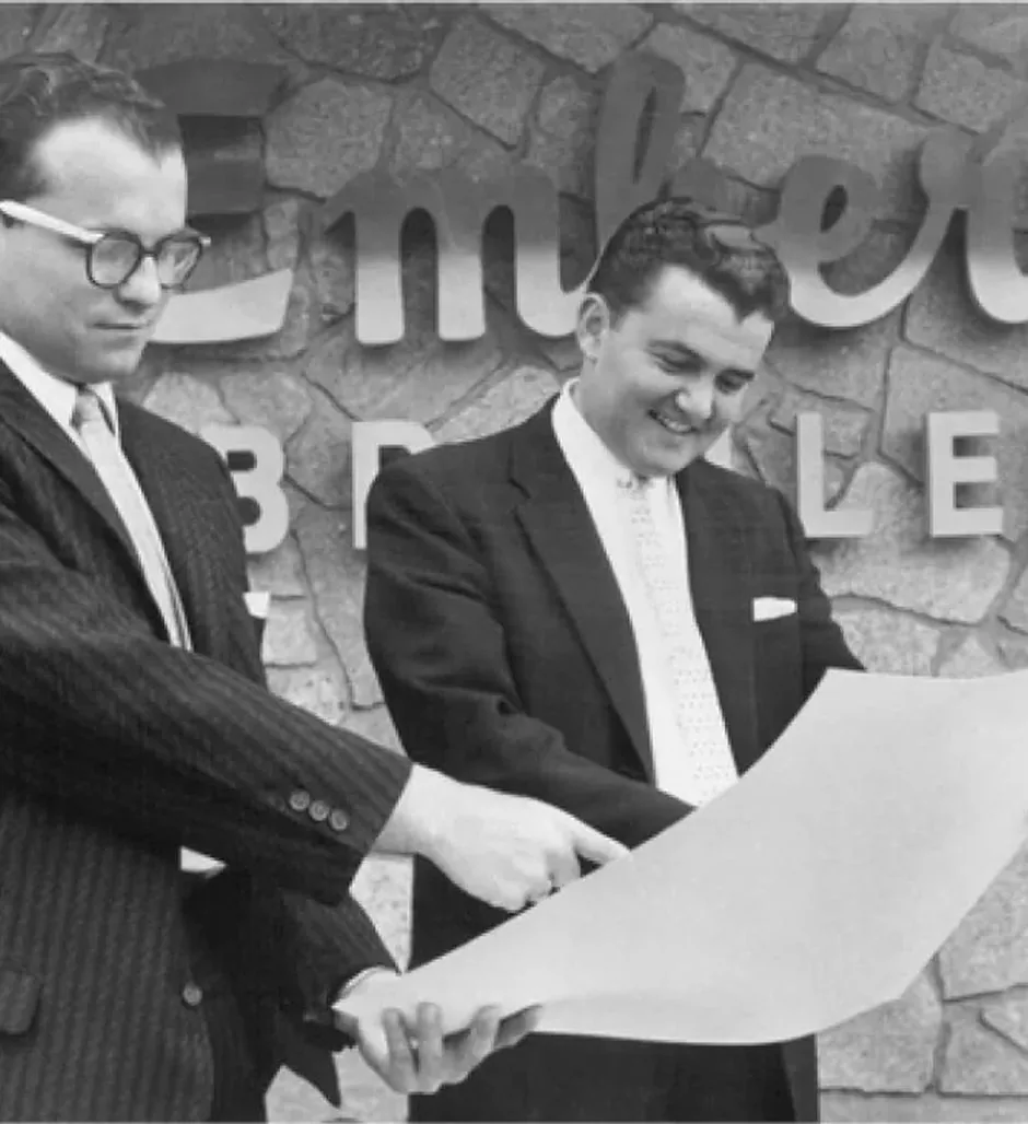 Archival photo of two men reviewing plans outside an Embers restaurant